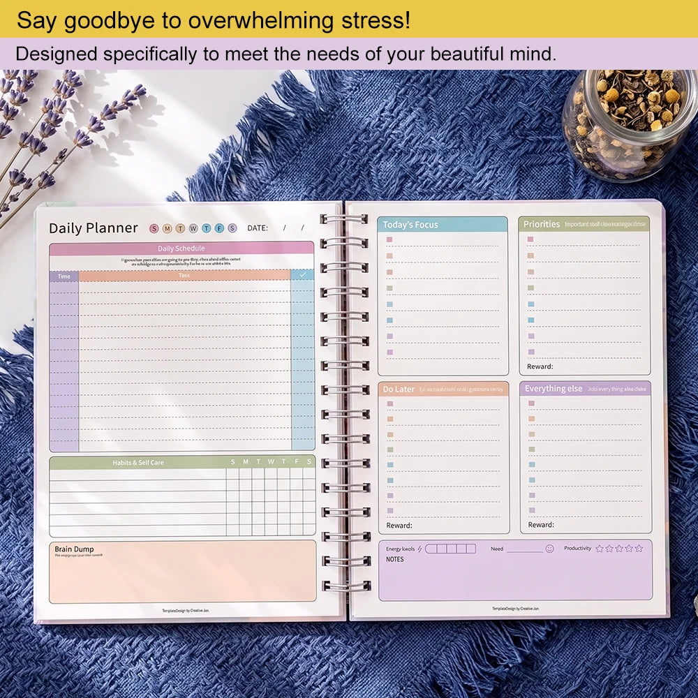An open spiral-bound daily planner with pastel-colored pages laid on a blue textured blanket, with lavender sprigs and a small jar of dried flowers nearby. Text at the top reads, 'Say goodbye to overwhelming stress! Designed specifically to meet the needs of your beautiful mind.