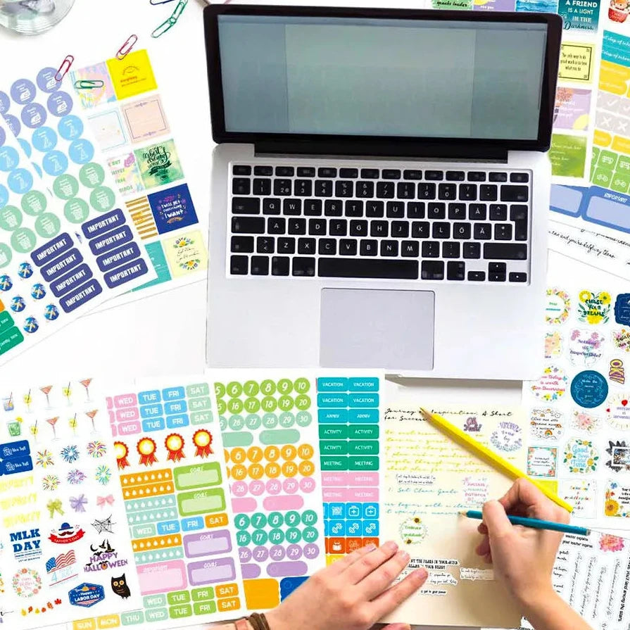  colourful planner sticker sheets arranged around a closed silver laptop.